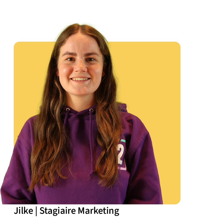 Jilke, stagiaire marketing bij Connect2Sports, in paarse hoodie met logo voor een gele achtergrond, lachend in de camera.